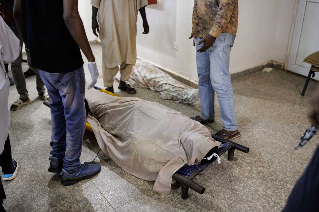 People surround the bodies of two shelling victims as they lie on a corridor floor.