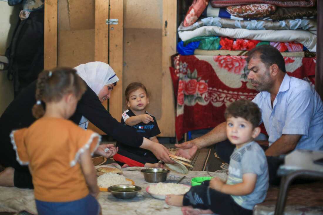 Suad Ali Al-Nidr serves dinner to her two daughters, her father and her nephew. They are seated on a cloth spread on the floor.