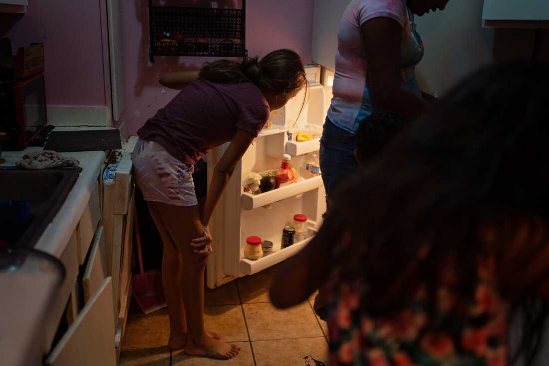 In this photo, Emilia Lopez's 12-year-old daughter has opened the refrigerator door and is peering inside. The shelves on the door hold jars and bottles.