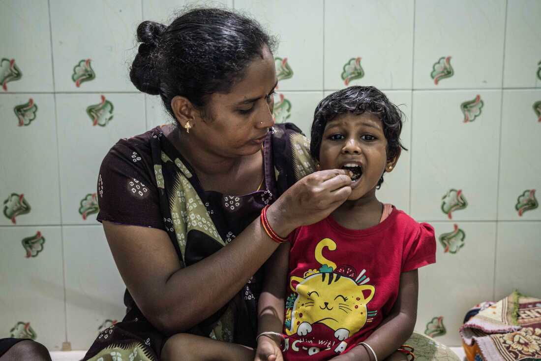 In this photo, Lakshmi holds food in her fingers that she's putting into the open mouth of her daughter, Sakshi.