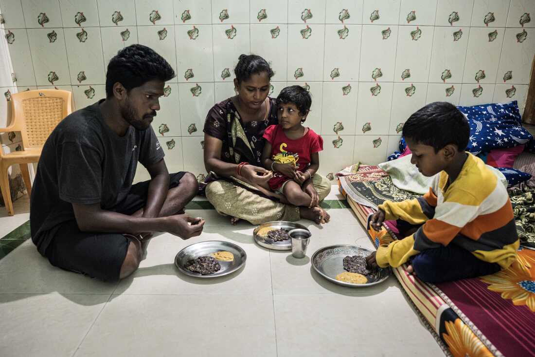 In this photo, Srinivasan, Lakshmi and their son sit cross-legged on the tile floor of their home. Daughter Sakshi sits in her mother's lap. Steel plates are on the floor, each containing a millet-based flatbread and a serving of chutney.