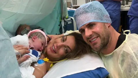 Andrea Byrne / Y Lolfa Andrea and Lee in the operating theatre pose for a photograph with their newborn daughter Jemima in 2019