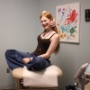 Veronica, 17, is a teen with long, straight red hair, wearing a camisole top, jeans and necklaces. She's sitting cross-legged on a medical exam table, smiling.