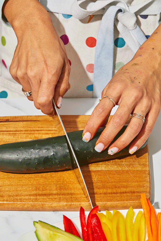 Four photographs show the process of creating cucumber veggie rolls. The instructions are as follows: Halve two large cucumbers widthwise. Using an apple corer, remove the center of the cucumbers. Stuff the hollow cucumbers with slices of avocado, red bell pepper, yellow bell pepper and carrot until they’re filled to the brim. Then slice your veggie-filled cucumbers into half-inch rounds.