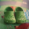 This photo shows a pair of green Crocs shoes resting on a colorful rug.