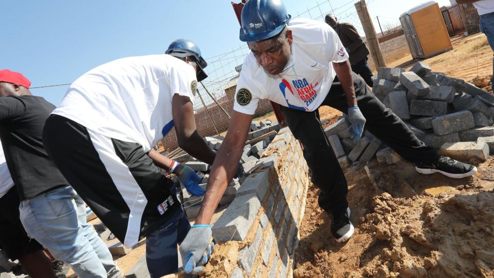 Dikembe Mutombo (right) uses a trowel to put down cement on a low wall while participating in building work as part of a Basketball Without Borders Africa program in a township in Johannesburg in August 2018