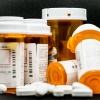 A smattering of loose prescription pills surround bottles and U.S. currency.