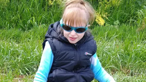 Lisa Hawker Jaydi wearing a dark blue gillet over a light blue fleece with her hair tied up in a pony tail and wearing a pair of sunglassess.