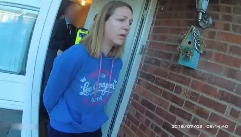 Cheshire Constabulary Lucy Letby, with long straight hair and a blue hoodie, is led from her front door in handcuffs.