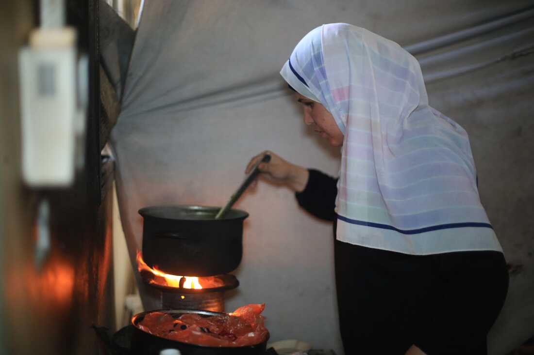 In this photo, Suad Ali Al-Nidr stirs a pot of mulukhiyah, a soup made from jute leaves. Orange flames heat the pot from underneath.