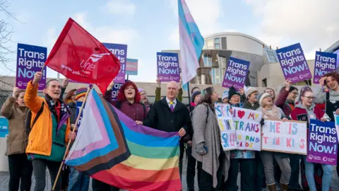 Getty Images Trans rights campaigners outside the Scottish Parliament, holding up a flag in their colours, and placards reading "trans rights now" and "cherish trans kids"