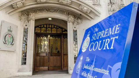 Getty Images Entrance to the Supreme Court in London, a white brick building covered in ornate carvings, including a big blue sign reading "the Supreme Court"