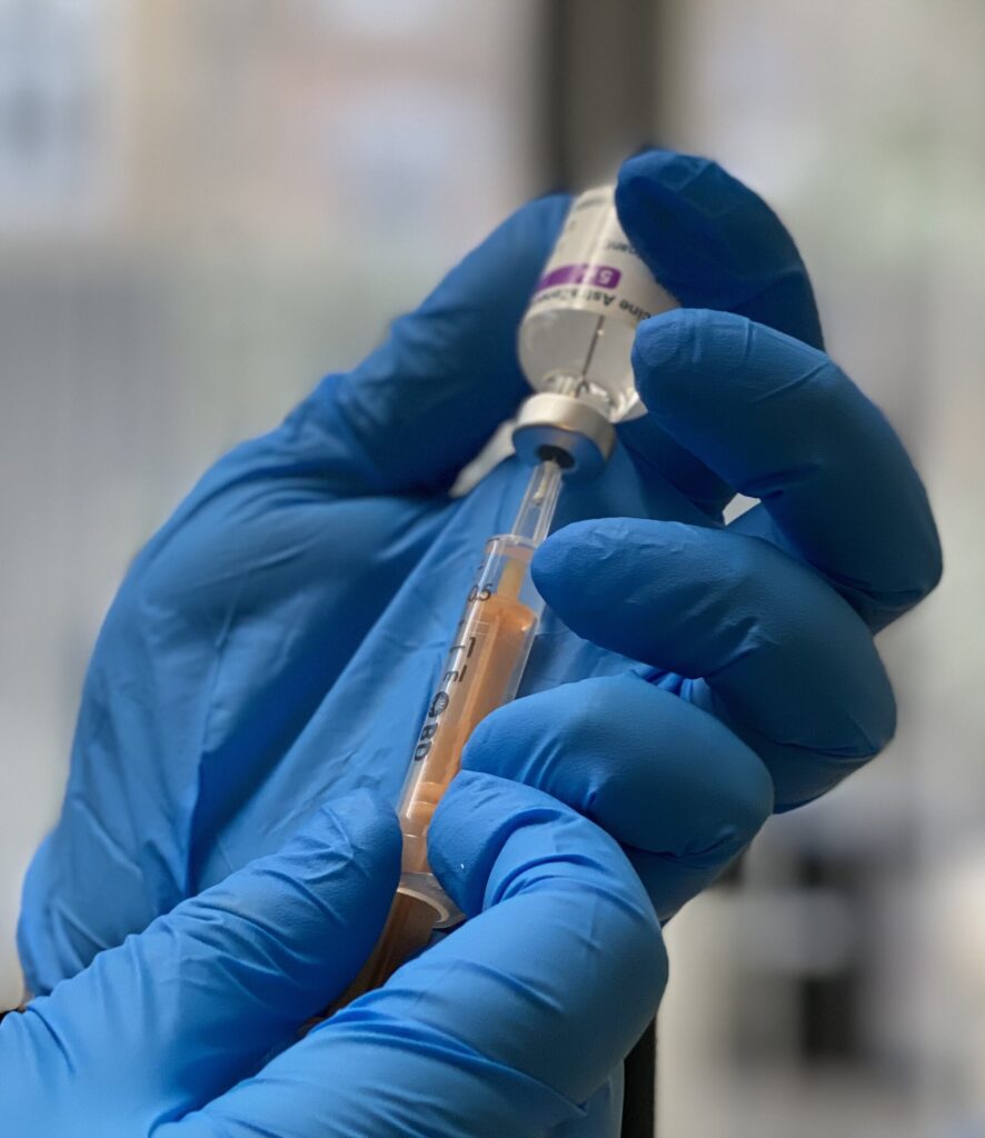 Blue-gloved hands holding a small vial and a syringe containing an amber-colored liquid.