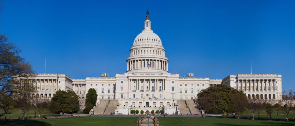 A wide exterior view of the US Capitol building in Washington, with its dome centered above the lawn.