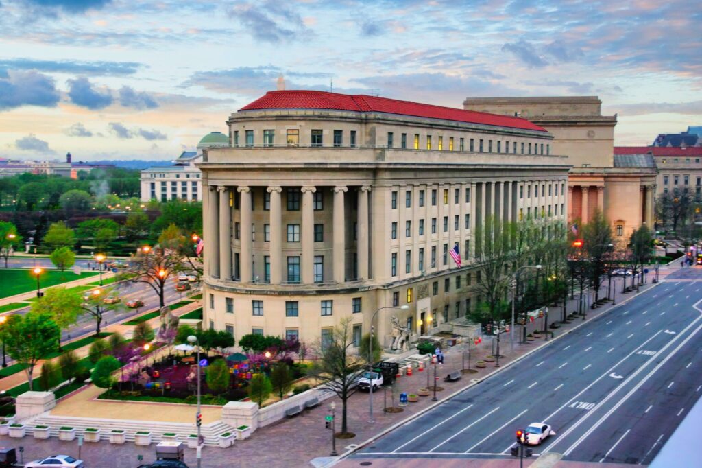 The large neoclassical Federal Trade Commission headquarters building beside a broad Washington street, with small vehicles and pedestrians visible below.